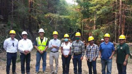 Legislators in hard hats standing in a forested area
