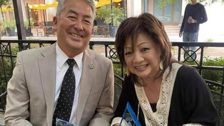 Assemblymember Muratsuchi sitting on a park bench with Maeley Tom while holding awards they just received