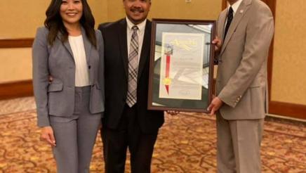 Assemblymember Muratsuchi stands to pose with the owners of Roxas Law and the framed certificate they received for being his district's Small Business of the Year