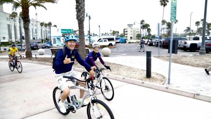 Assemblymember Muratsuchi does a hang ten gesture while riding his bike with others