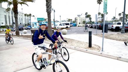 Assemblymember Muratsuchi does a hang ten gesture while riding his bike with others