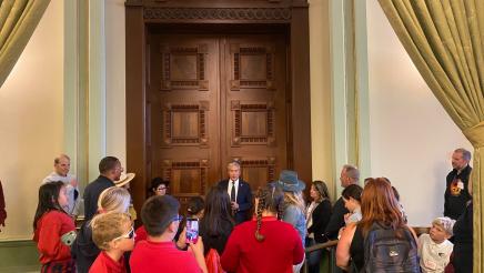 Asm. Muratsuchi speaking to students, standing in front of Assembly Chamber doors