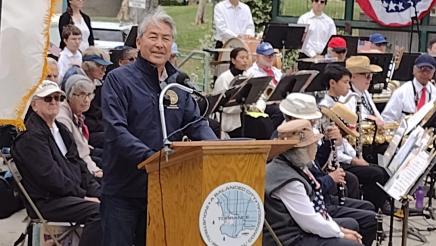 Asm. Muratsuchi on stage at podium, with band in background, speaking