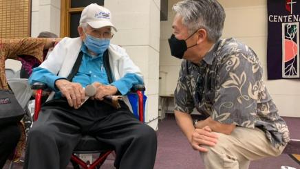 Assemblymember Muratsuchi kneels down to speak with an senior citizen attendee. 