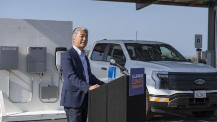 Assemblymember Al Muratsuchi speaks at a podium with an electric truck in the background.