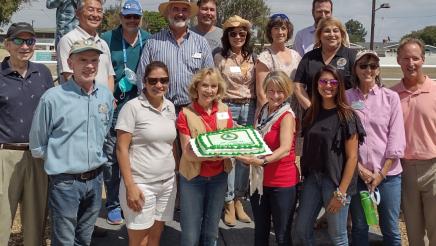 Assemblymember Al Muratsuchi stands for a group photo who are holding a large green cake. 