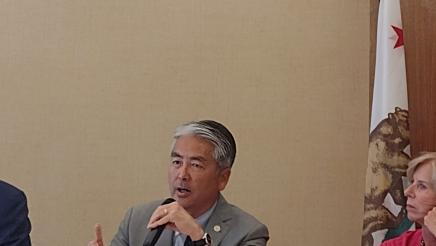 Asm. Muratsuchi seated at table with microphone, speaking