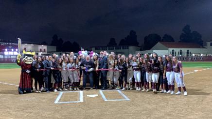 Group photo with softball players and volunteers, with ribbon being cut at center