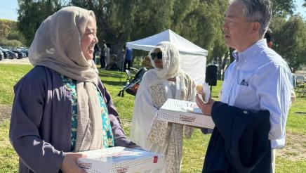 Asm. Muratsuchi speaking with attendee, both holding Krispy Kreme doughnut boxes
