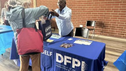 Department of Financial Protection & Innovation staffer at table, distributing materials