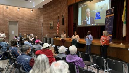 Guest speakers speaking to attendees, with slideshow displayed on large screen