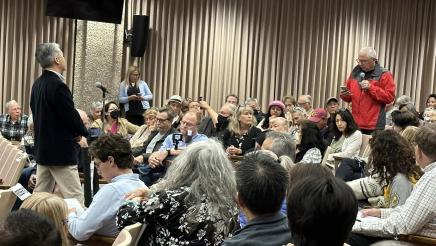 Standing attendee asking question as Asm. Muratsuchi and large audience listen on
