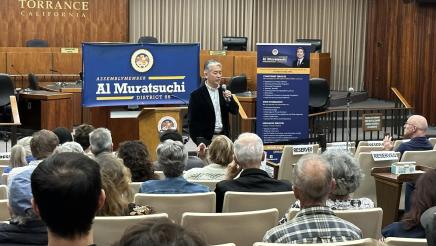 Asm. Muratsuchi standing at head of room with microphone, speaking to attendees
