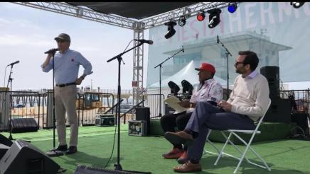 Asm. Muratsuchi standing on stage, speaking, as Mayor Jackson and Sen. Allen listen on