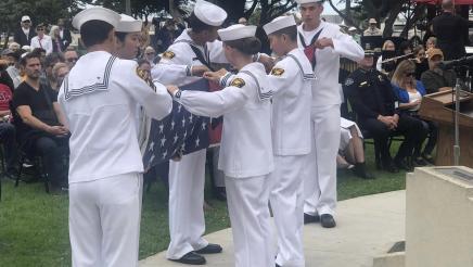 U.S. flag being folded by service members dressed in white