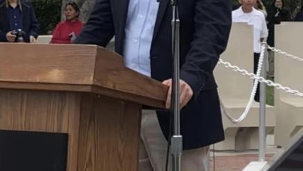 Asm. Muratsuchi standing at podium with microphone, speaking to attendees