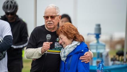 South Bay Bicycle Coalition member holding microphone, embracing Rabbi Gila Katz