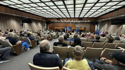 Asm. Muratsuchi standing at head of room with microphone, speaking to large audience