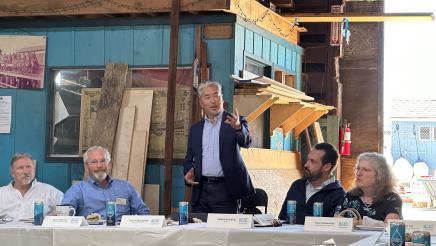 Asm. Muratsuchi reaches out one hand while standing and speaking to participants seated at tables