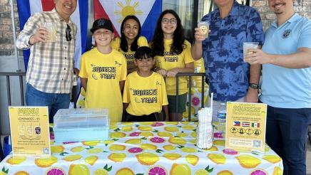 Asm. Muratsuchi raising a cup at lemonade booth with students and adults