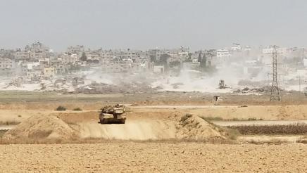 Tank in desert on hill, overlooking many buildings in the distance