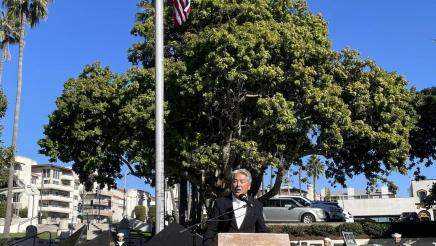 Asm. Muratsuchi at podium, speaking, in front of the Veterans Memorial