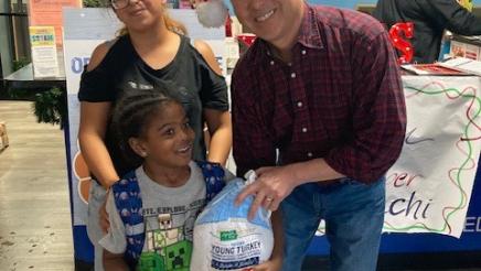 Asm. Muratsuchi distributing turkey to child with mother standing behind