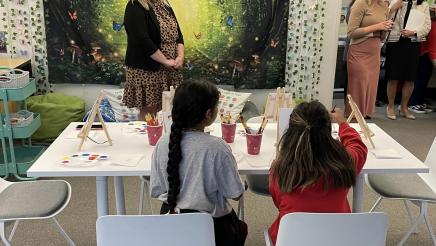 Children creating artwork on table and tour participants look on