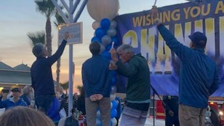 Asm. Muratsuchi witj others onstage and firefighter on ladder lights a large Menorah