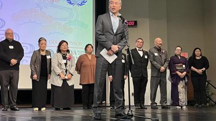 Asm. Muratsuchi at microphone onstage with Okinawa Association members in background
