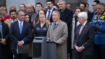 Asm. Muratsuchi at podium, speaking, with officials and others at sides and at back