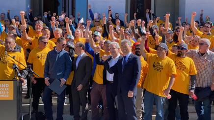 Asm. Muratsuchi and multiple participants wearing yellow shirts holding up arms