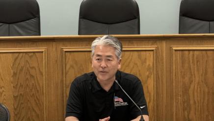 Asm. Muratsuchi seated at table, speaking into microphone
