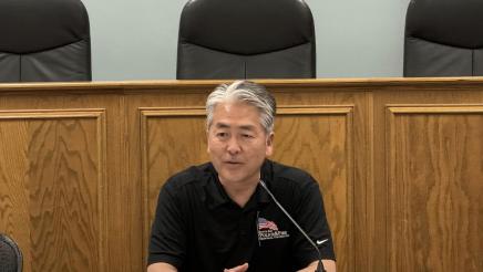 Asm. Muratsuchi seated at table, speaking into microphone