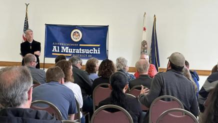 Asm. Muratsuchi standing at head of room, listening, as audience member speaks