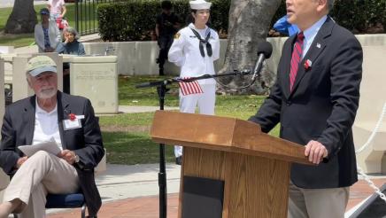 Asm. Muratsuchi at podium, speaking, with sailor in uniform listening on in background