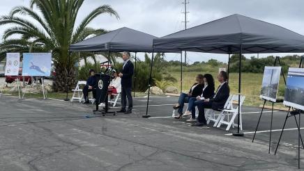 Asm. Muratsuchi at podium, speaking, as other guests sit under canopy tents and listen on