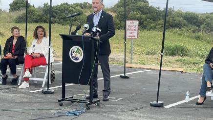 Asm. Muratsuchi at podium, speaking, with wooded area in background