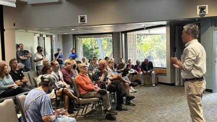 Asm. Muratsuchi speaking into microphone while seated attendees listen on