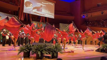 Performers wearing red onstage, dancing and waving large red flags