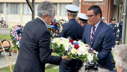 Asm. Muratsuchi and attendee handling a large wreath of flowers