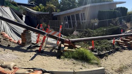 Damaged house within sunken landslide area, with temporary pipeline in front