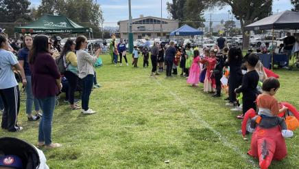 Halloween costume contestants lined up on grass, with parents looking on