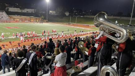 Band members and fans in stadium bleachers, overlooking field