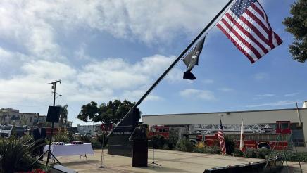 Veteran standing at podium, speaking, with large flag and pole overhead