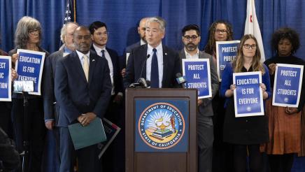 Asm. Muratsuchi at podium, with Superintendent Thurmond standing at left and others holding signs