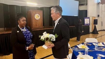 Asm. Muratsuchi holding a vase of flowers while speaking with an attendee