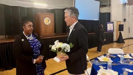 Asm. Muratsuchi holding a vase of flowers while speaking with an attendee