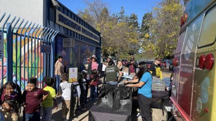 Bookmobile, tables filled with bags, and children in front of an elementary school