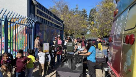 Bookmobile, tables filled with bags, and children in front of an elementary school